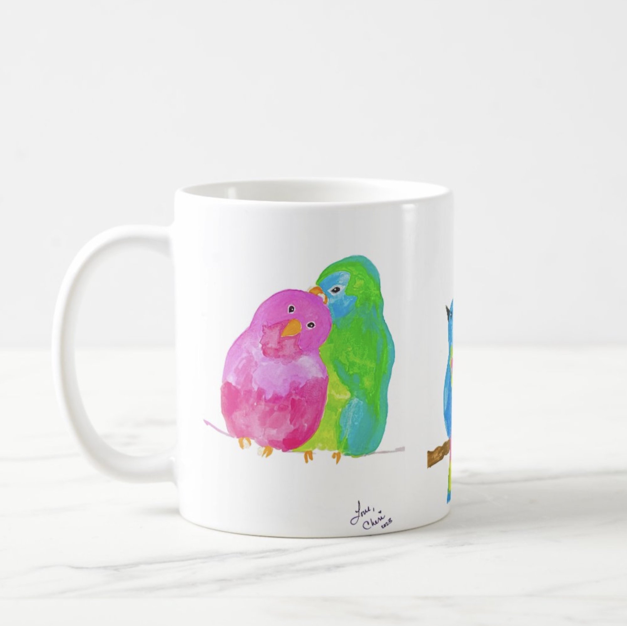White ceramic coffee mug featuring a watercolor illustration of two affectionate birds—one pink and one green—perched closely together, with a third partially visible blue bird on the side; artwork signed “Love, Cheri 2025” near the base.